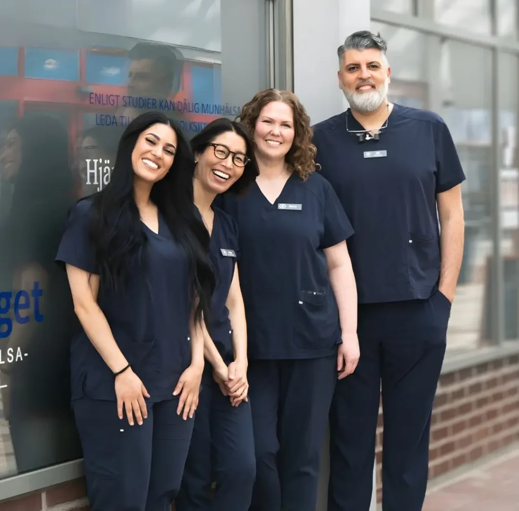 Four medical professionals in navy scrubs posing outside a clinic, smiling at the camera.